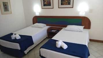 Een hotelkamer met twee eenpersoonsbedden, elk met een blauwe sprei en witte kussens, en een houten hoofdeinde. Boven de bedden hangen afbeeldingen in lijsten.