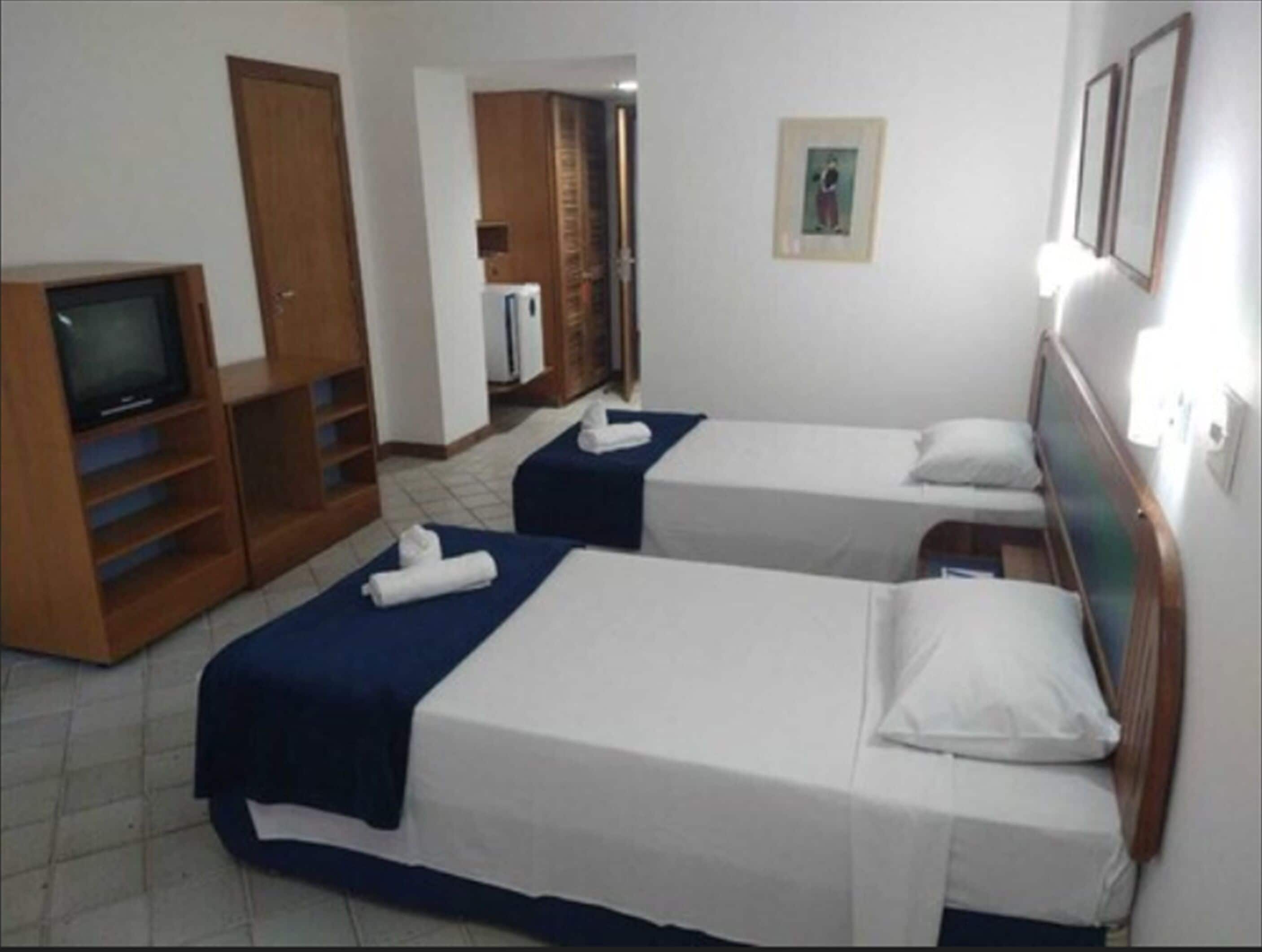 Une chambre d’hôtel avec deux lits simples, une télévision, une armoire et une petite kitchenette.