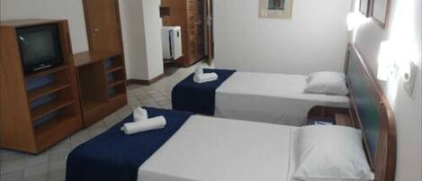 A hotel room with two single beds, a TV, a wardrobe, and a small kitchenette.