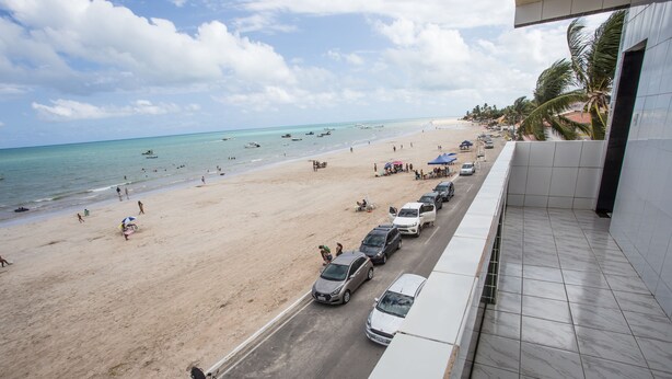 A beach view from a balcony with a row of parked cars and a motorcycle on the street. - Pousada Vela Mar (Maragogi)