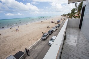 A beach view from a balcony with a row of parked cars and a motorcycle on the street. - Pousada Vela Mar (Maragogi)