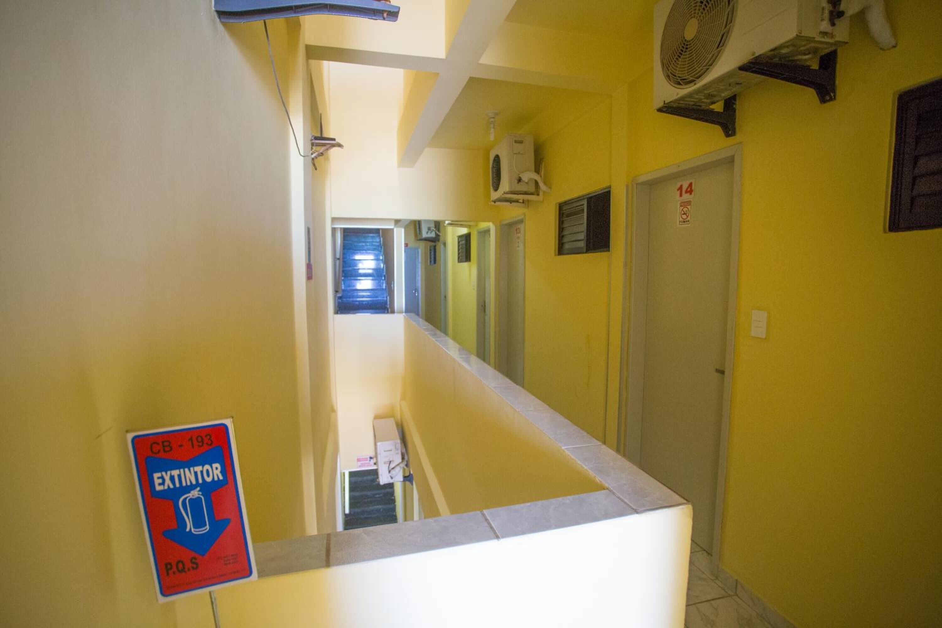 A narrow hallway with yellow walls, a CB-193 extinguisher sign, a white door with the number 14, and a ceiling fan.