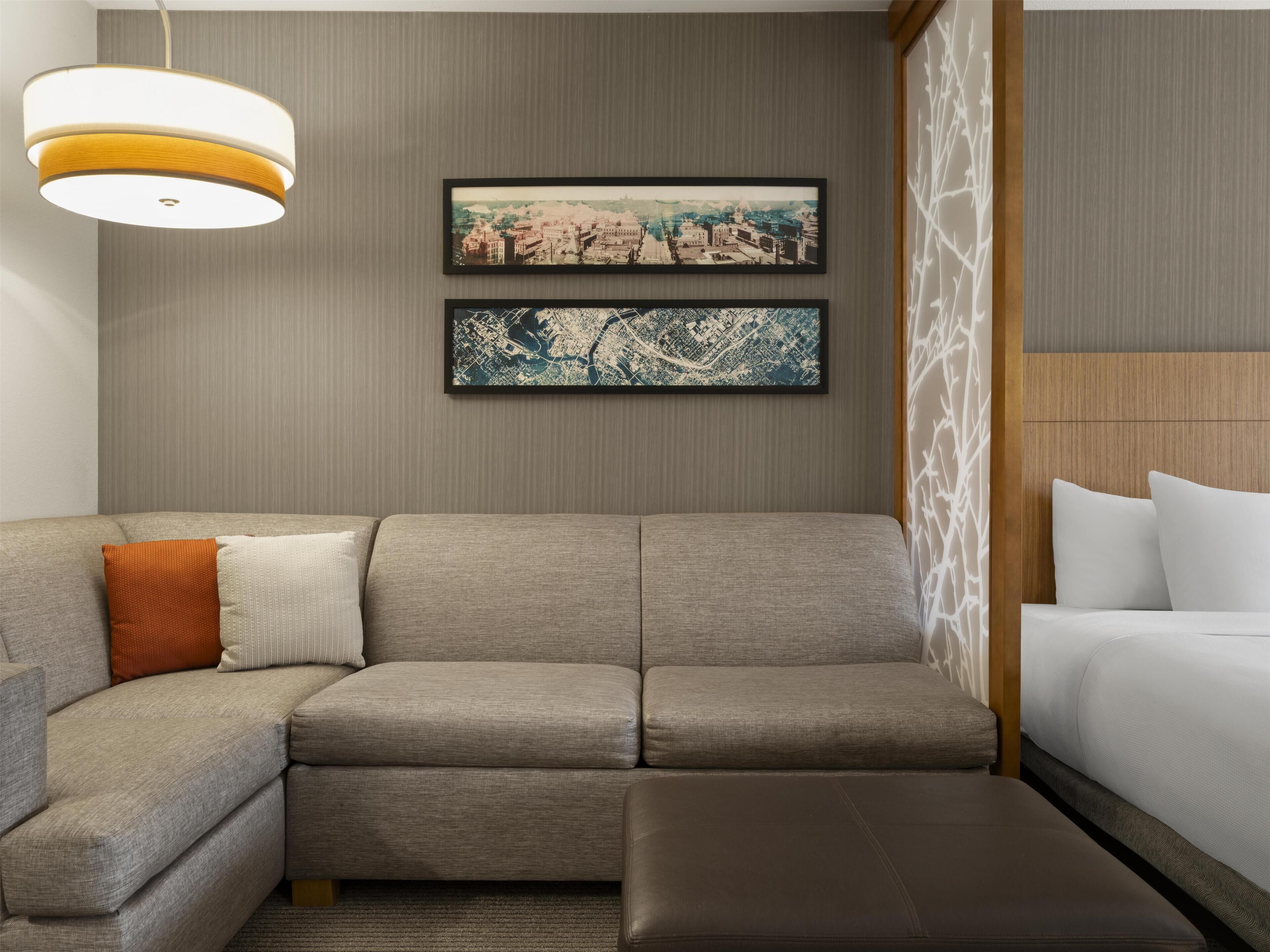 Une chambre d’hôtel moderne avec un canapé d’angle, un lit et deux photographies encadrées représentant des vues de la ville, accrochées au mur.