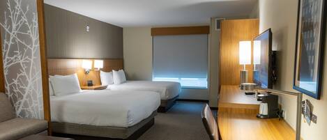Een hotelkamer met twee bedden, een bureau met lamp, een stoel, een televisie en een raam met jaloezieën.