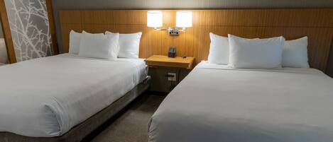 A hotel room with two beds, each with white linens, a wooden headboard, and a nightstand with a lamp.