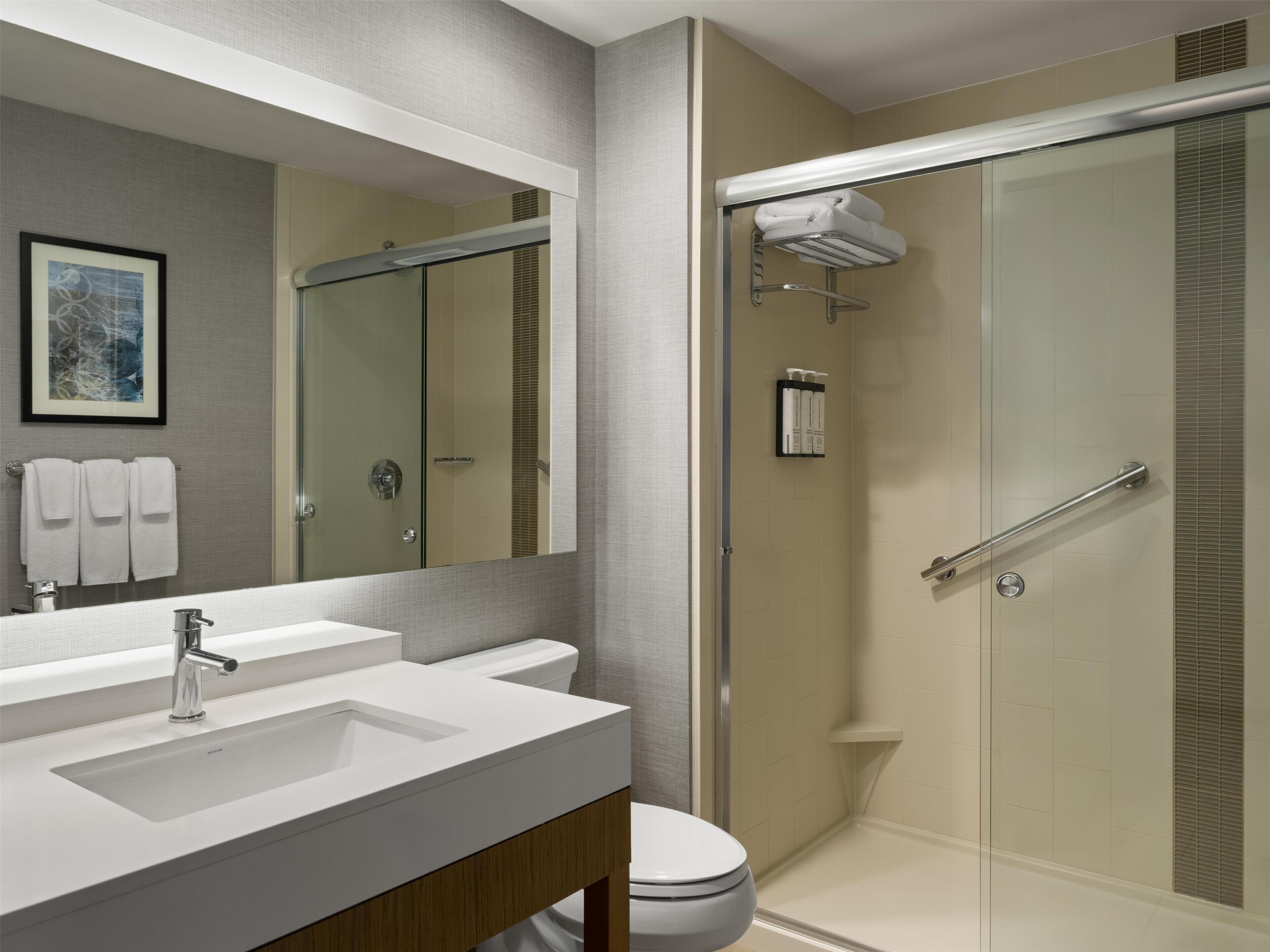 Une salle de bain moderne avec un grand miroir, deux lavabos, des toilettes et une douche séparée par une paroi de verre.