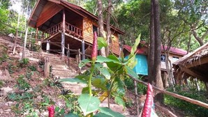 A wooden house with a porch, surrounded by trees and vegetation. - Jungle Hill Beach Bungalow (Nuea Khlong)