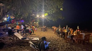 An outdoor seating area with tables and chairs, surrounded by trees and illuminated by string lights. - Jungle Hill Beach Bungalow (Nuea Khlong)
