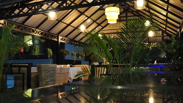 A spacious indoor area with a glass ceiling, wicker furniture, and potted plants.