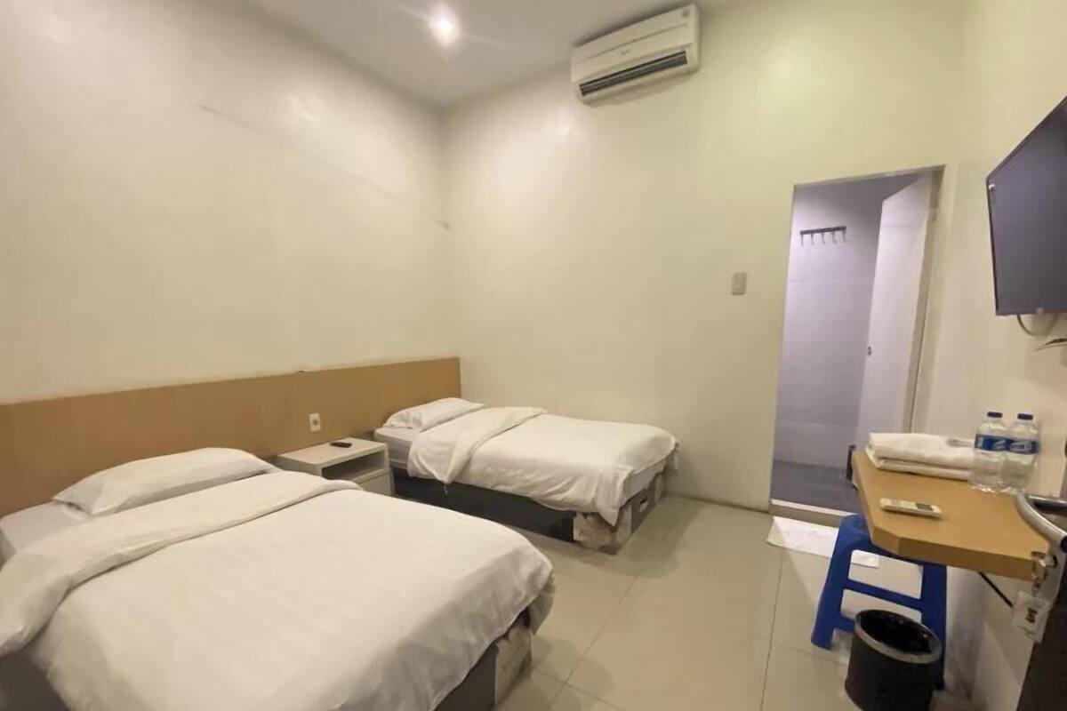 Una habitación de hotel con dos camas, un escritorio, una silla, un cubo de basura y un equipo de aire acondicionado.