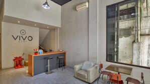 A modern hotel lobby with a reception desk, a sofa, a dining area, and a staircase. - Vivo Stay (Medan)