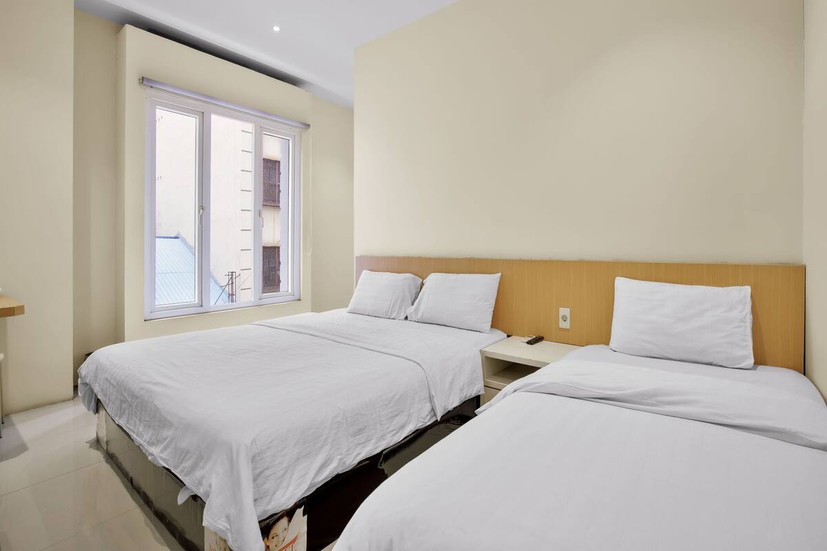 Habitación de hotel con dos camas, una ventana y un cabecero de madera.