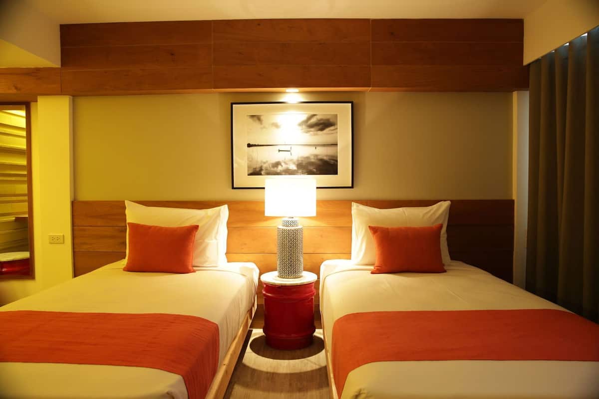 A hotel room with two beds, a nightstand with a lamp, and a framed picture on the wall.
