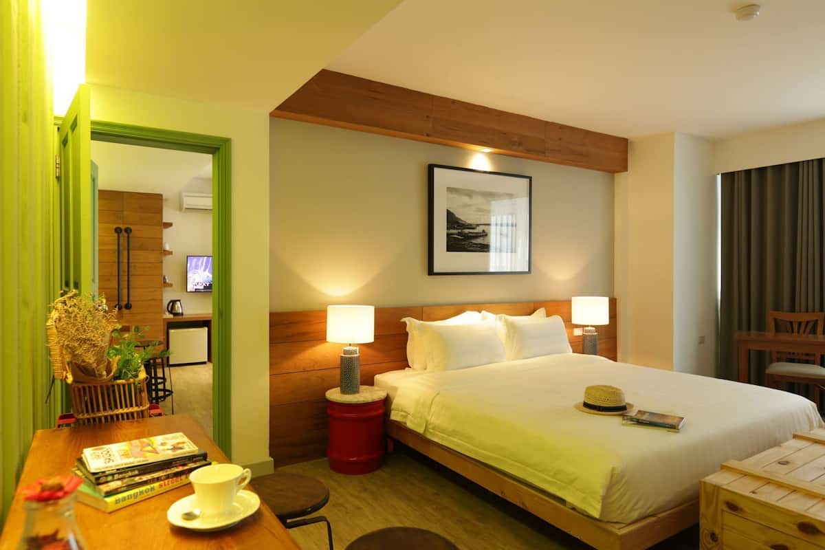 A hotel room with a bed, bedside lamps, a desk with a chair, a small table, and a television.