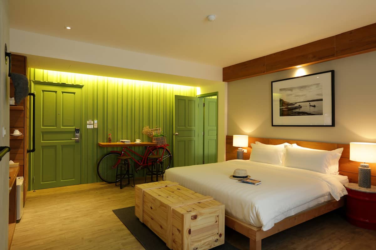 A hotel room with a bed, bedside lamps, a wooden headboard, a framed picture on the wall, and a green door.