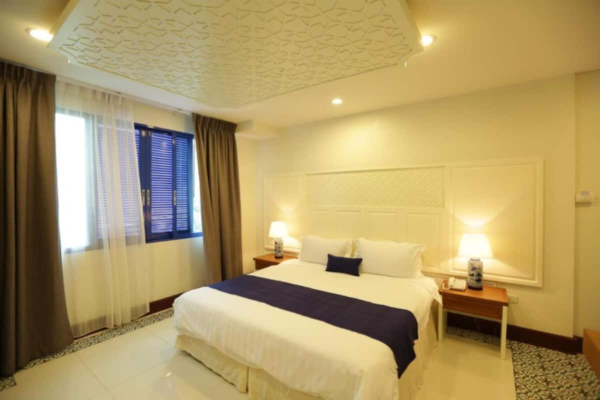 A hotel room with a large bed, two bedside tables with lamps, a headboard with a textured design, and a patterned rug on the floor.