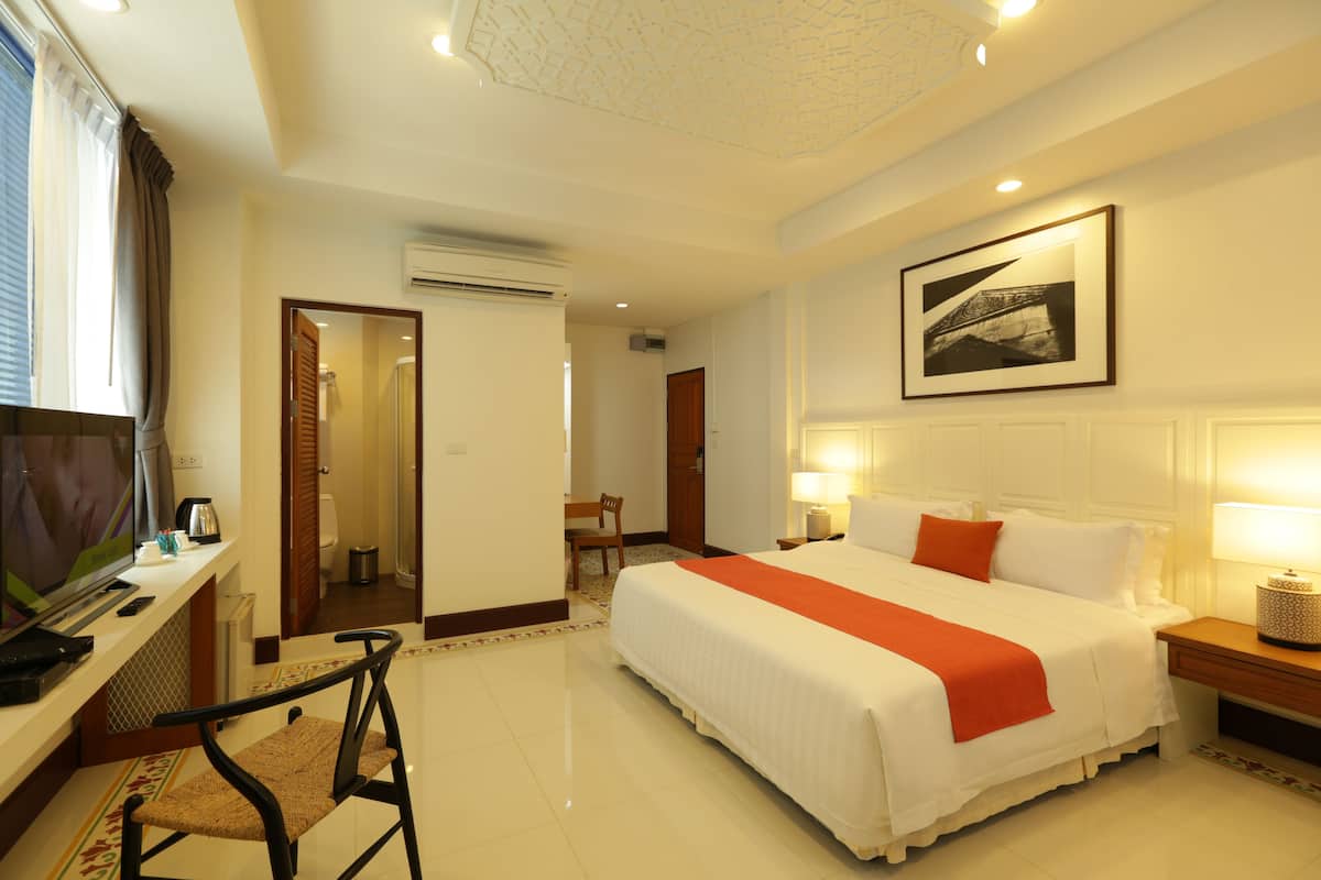 A hotel room with a bed, a desk with a television, a chair, and a bathroom visible through an open door.