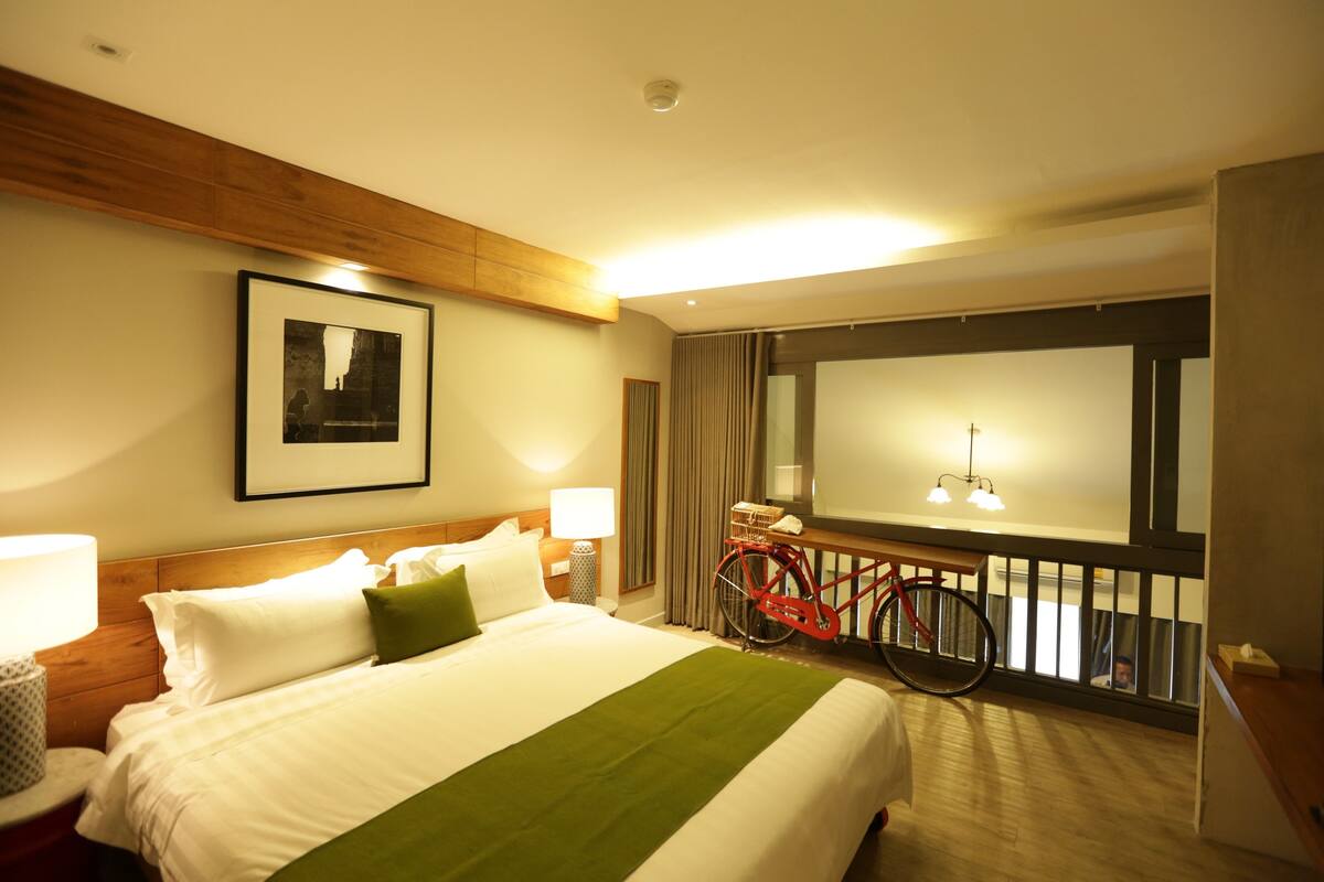 A hotel room with a bed, a bicycle, a window, and a mirror.