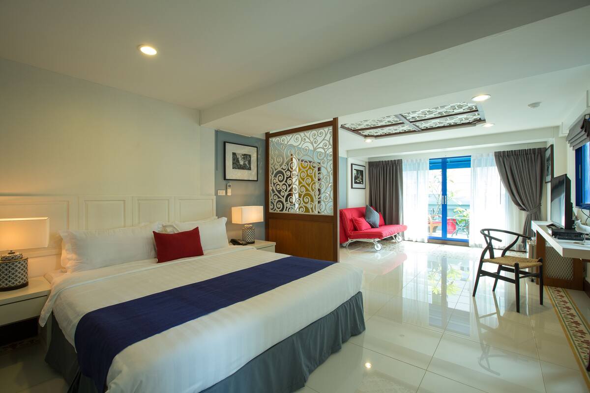 A hotel room with a large bed, a desk, a chair, and a view of the outdoors.