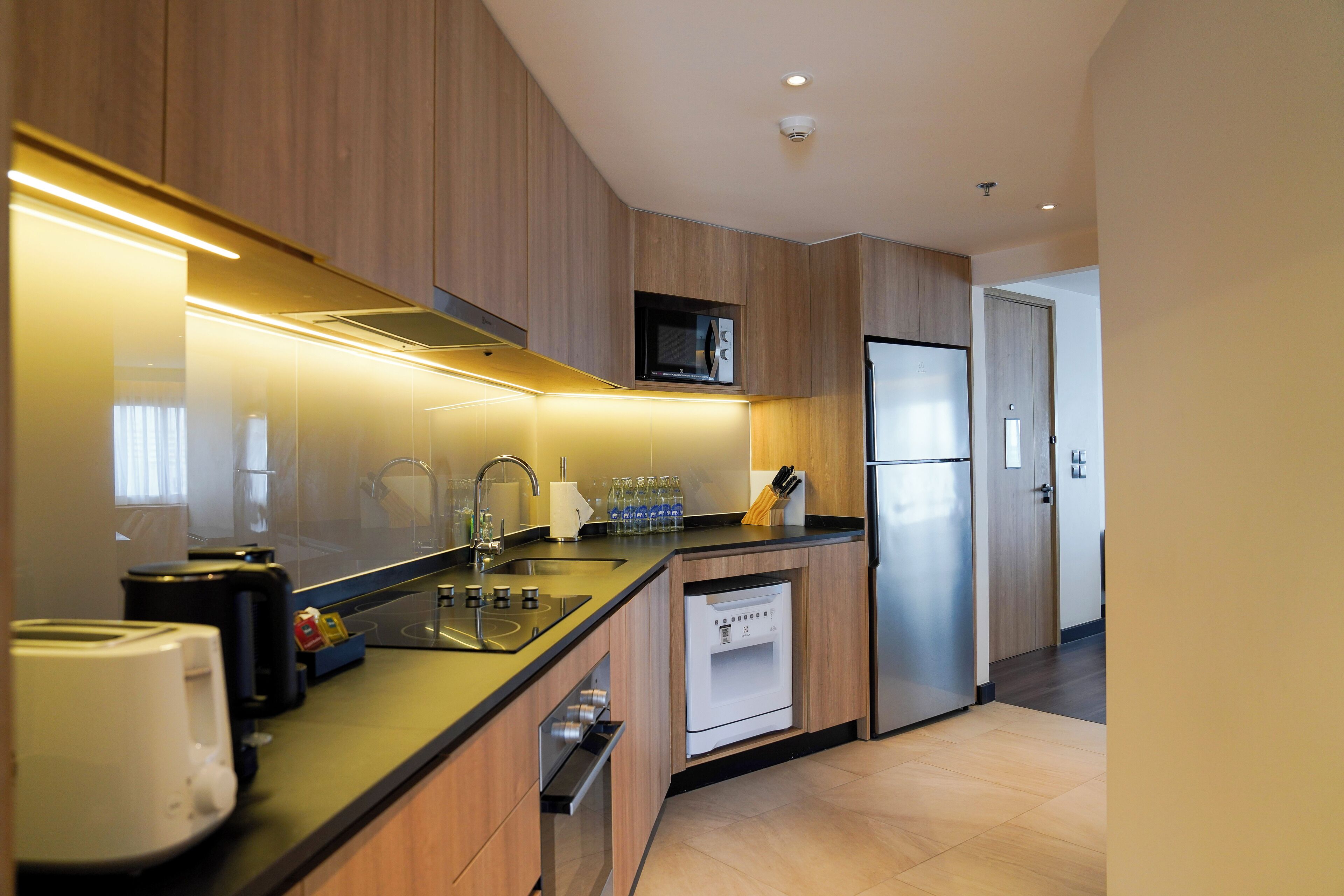 A modern kitchen with wooden cabinets, a stainless steel refrigerator, a microwave, and a dishwasher.