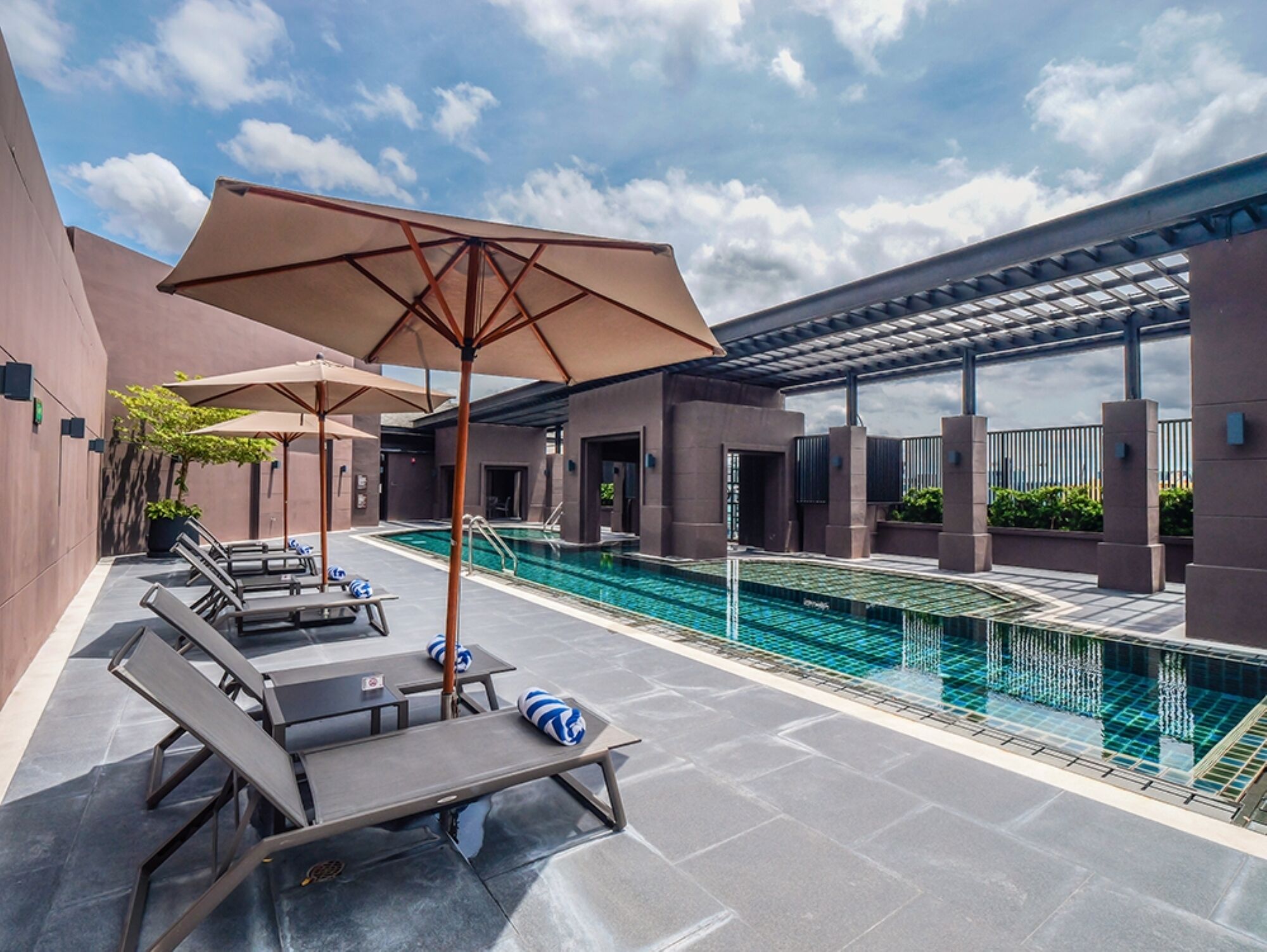 Un espace piscine aménagé sur le toit, avec des chaises longues et des parasols, entouré d’une architecture moderne.