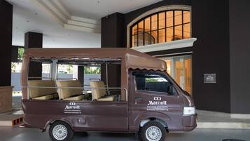 Een bruine bestelwagen met daarop 'Marriott Executive Apartments Bangkok Sukhumvit 50', geparkeerd voor een gebouw met een groot rondboogvenster.