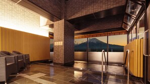 A modern lobby with a tiled floor, a seating area with wicker chairs, a large window with a mountain view, and a wooden wall. - HOTEL MYSTAYS Fuji Onsen Resort (Fujiyoshida)