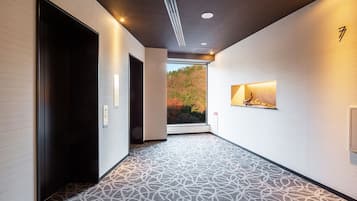 A hallway with patterned carpet, a dark elevator, and a wall-mounted light fixture.