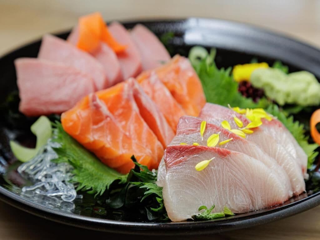 A plate of sashimi with salmon and tuna, garnished with green leaves and yellow flowers.