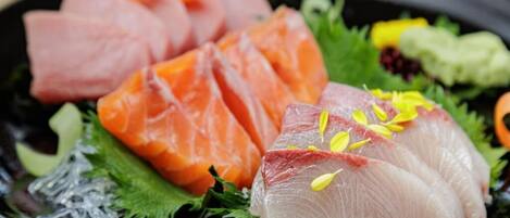 A plate of sashimi with salmon and tuna, garnished with green leaves and yellow flowers.