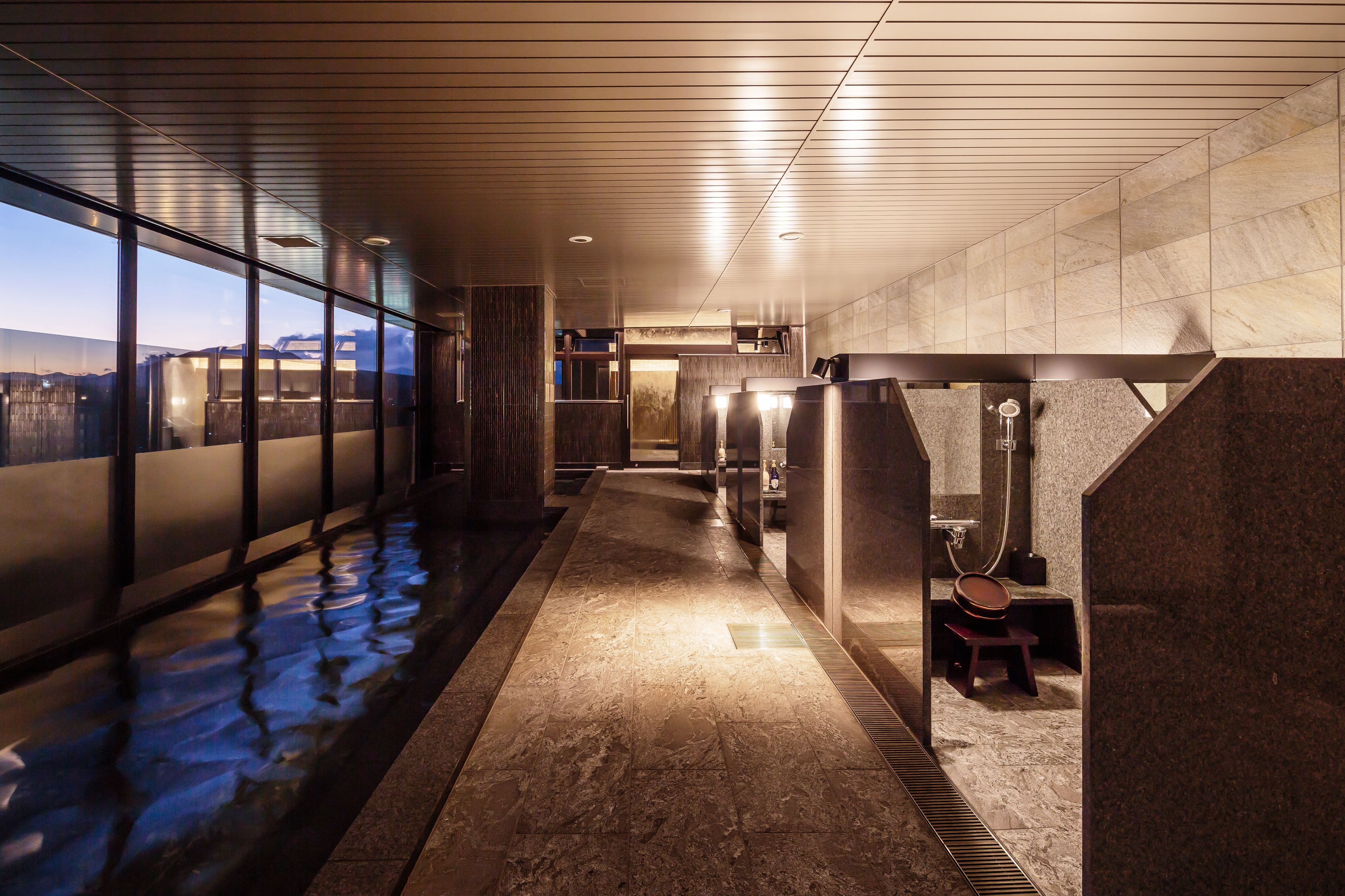 Un pasillo moderno de hotel con piso reflectante, separaciones de vidrio y vista a la ciudad.