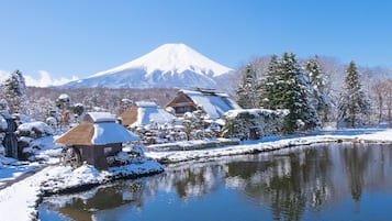 Uma aldeia japonesa tradicional com um lago coberto de neve, edifícios com telhados de palha e uma montanha nevada imponente ao fundo.