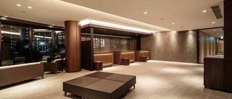 A modern hotel lobby with a reception desk, seating area, and large windows offering a city view.