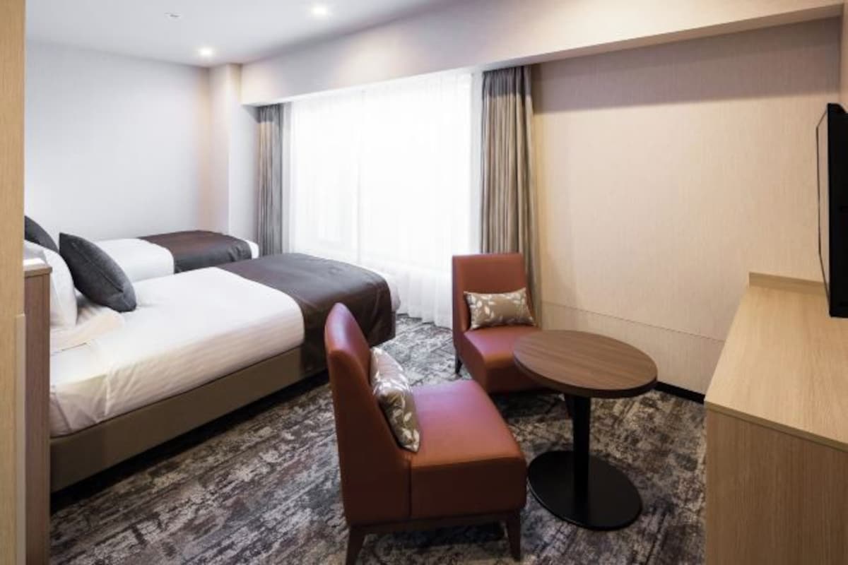 A hotel room with a bed, two armchairs, a small table, and a TV.