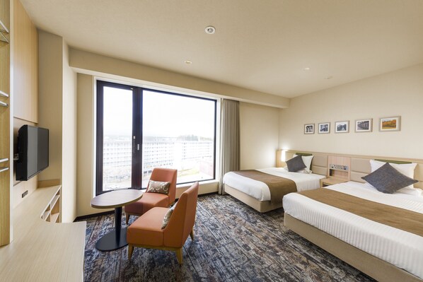 Habitación de hotel con dos camas, un escritorio, una silla y un ventanal grande.