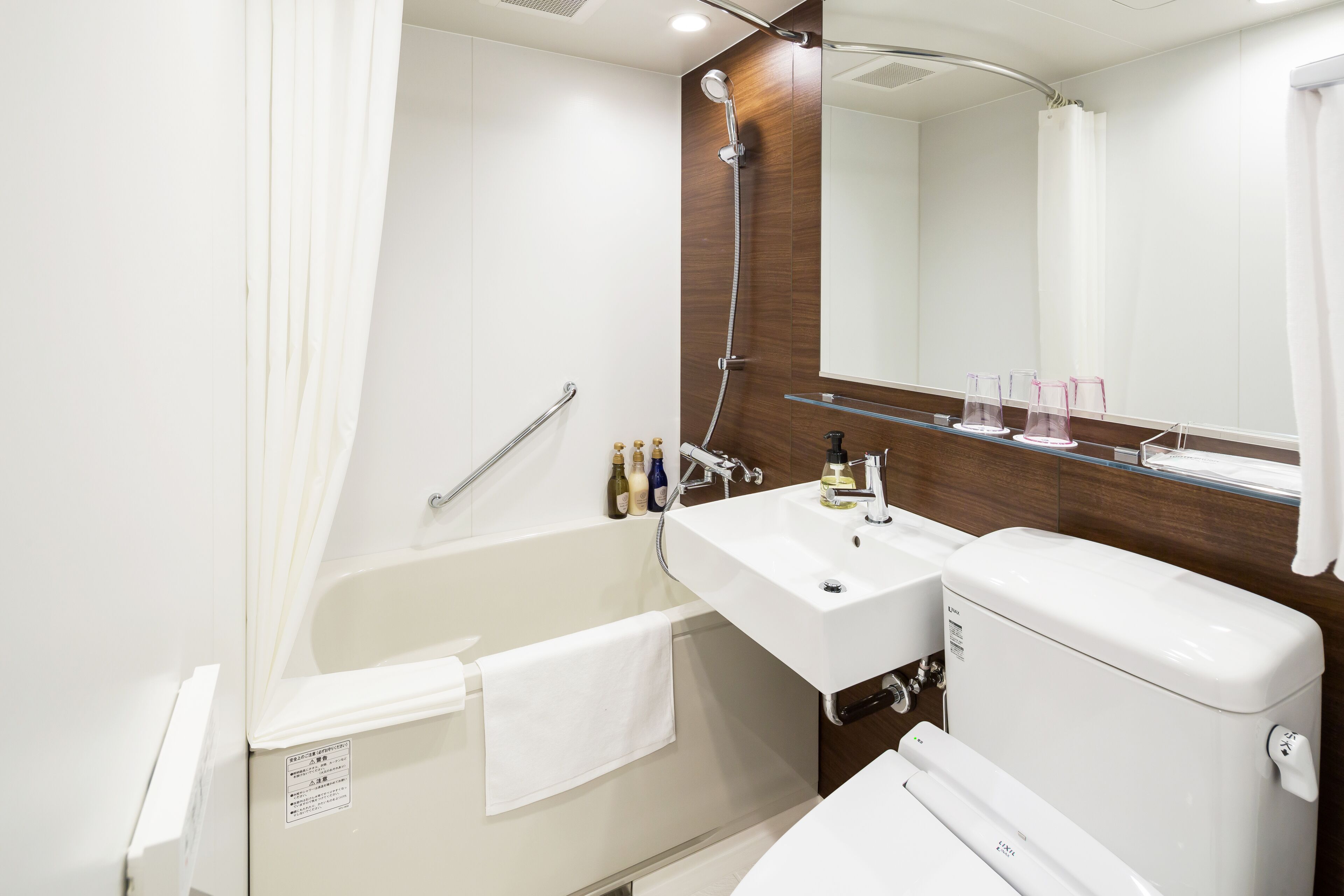Un baño moderno con bañera, lavabo e inodoro. Hay un cabezal de ducha sobre la bañera, un espejo sobre el lavabo y una toalla colgada al lado de la bañera.