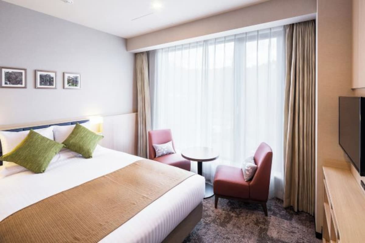 A hotel room with a large bed, two armchairs, a small table, and a TV.