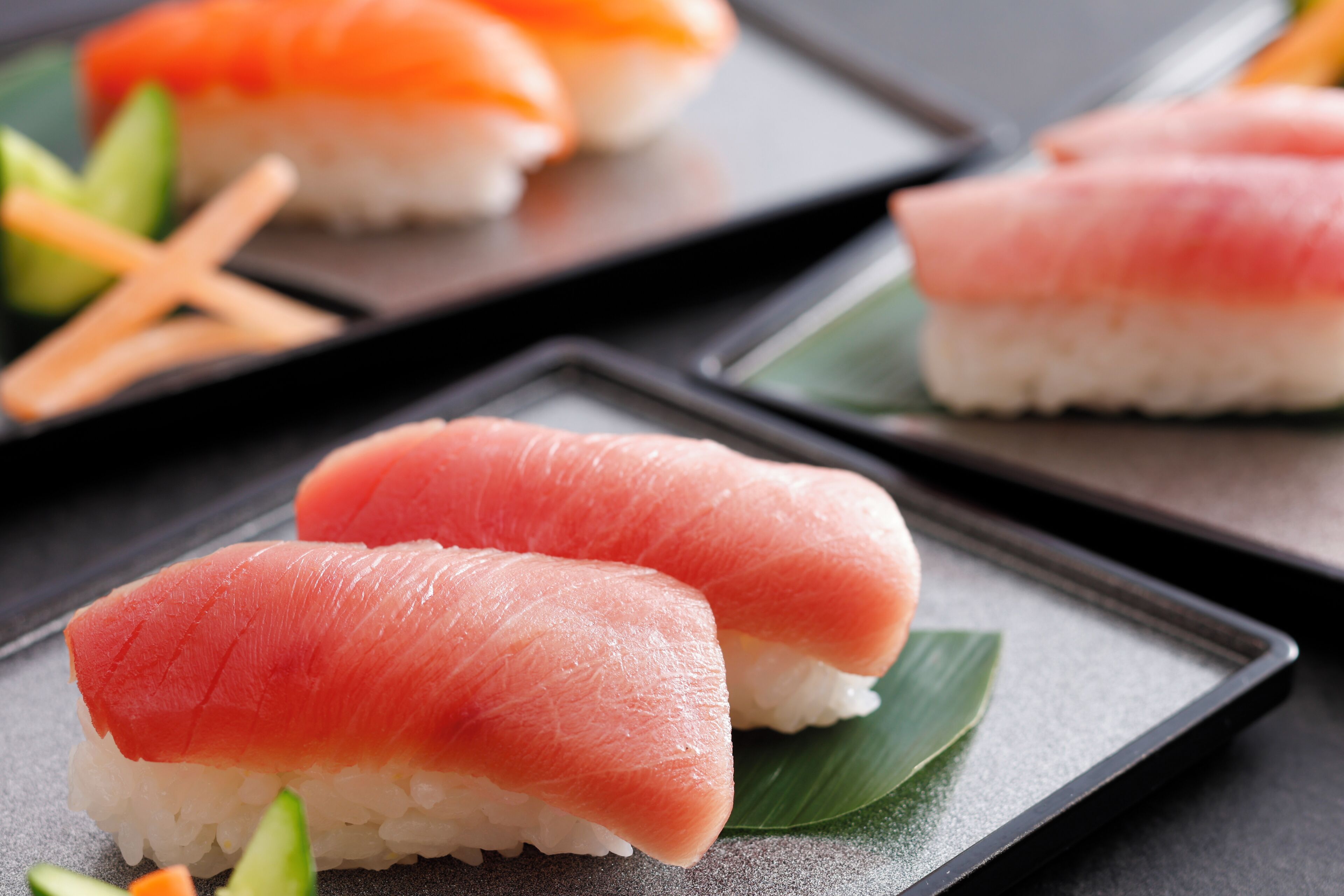 Sushi sobre um prato preto, decorado com uma folha verde.