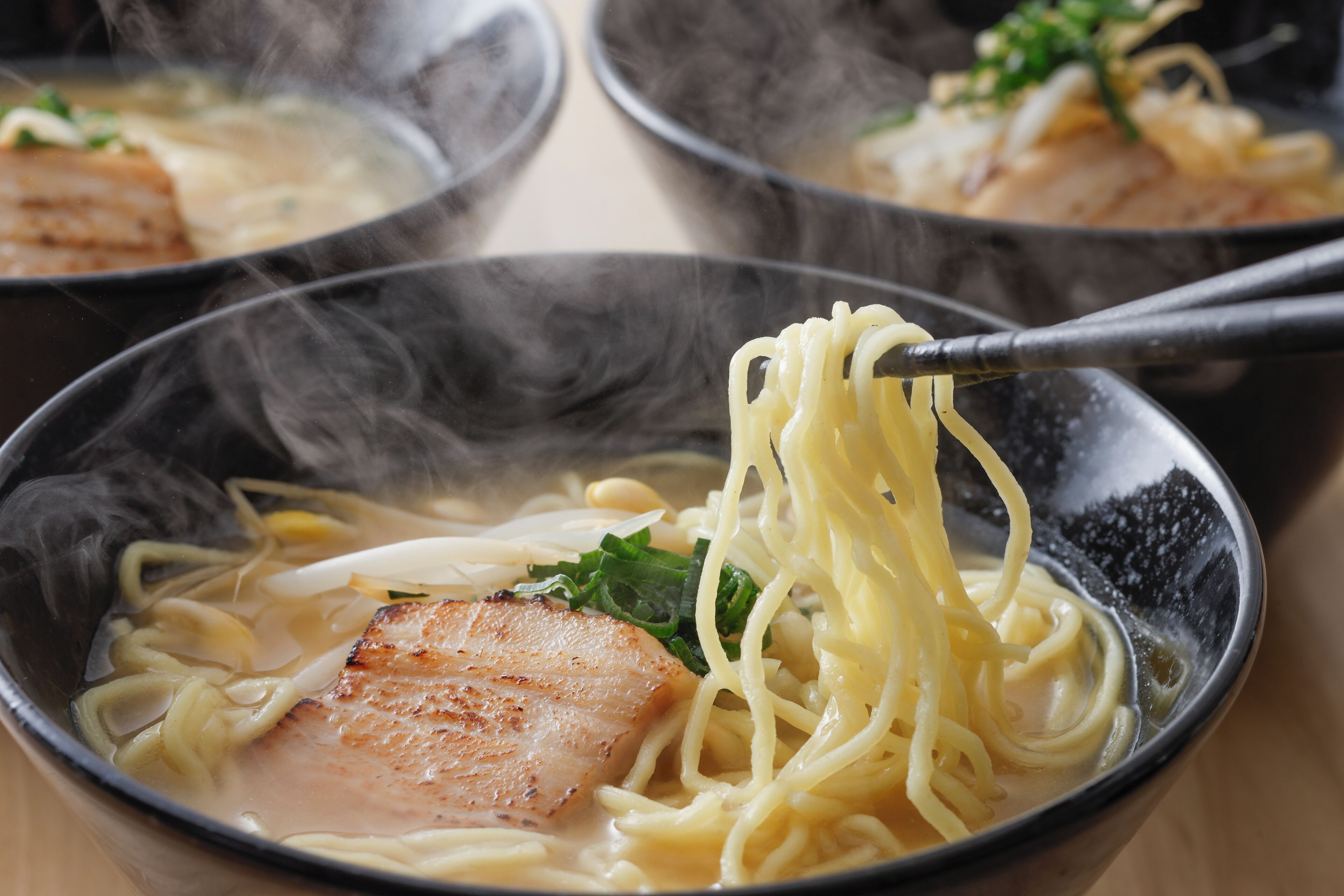 A bowl of ramen with noodles, a piece of meat, and green toppings.