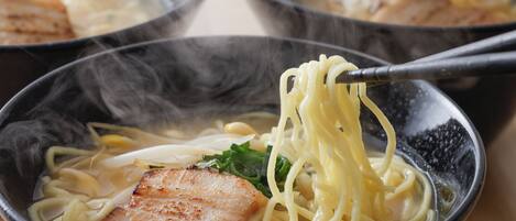 A bowl of ramen with noodles, a piece of meat, and green toppings.