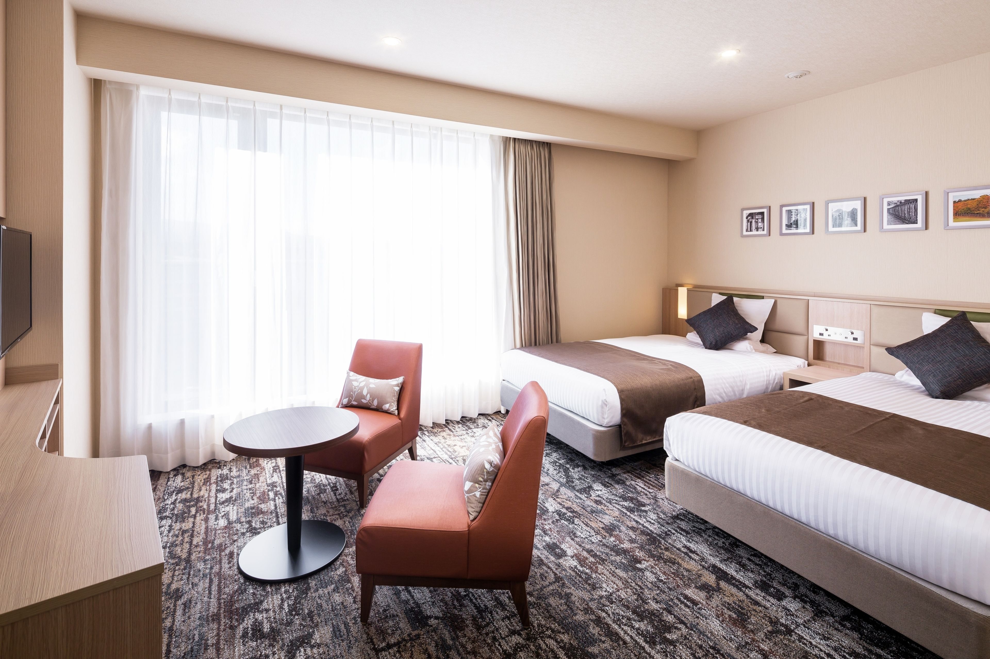 A hotel room with two beds, a sofa, a small round table, and a TV.