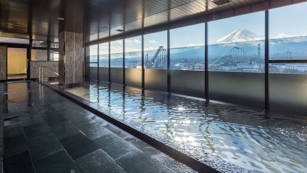A modern indoor pool with a view of a mountain and industrial structures. - HOTEL MYSTAYS Fuji Onsen Resort (Fujiyoshida)