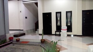 A hotel lobby with a tiled floor, black doors, a staircase, and potted plants. - Jaya Phita Guest House (Kupang)