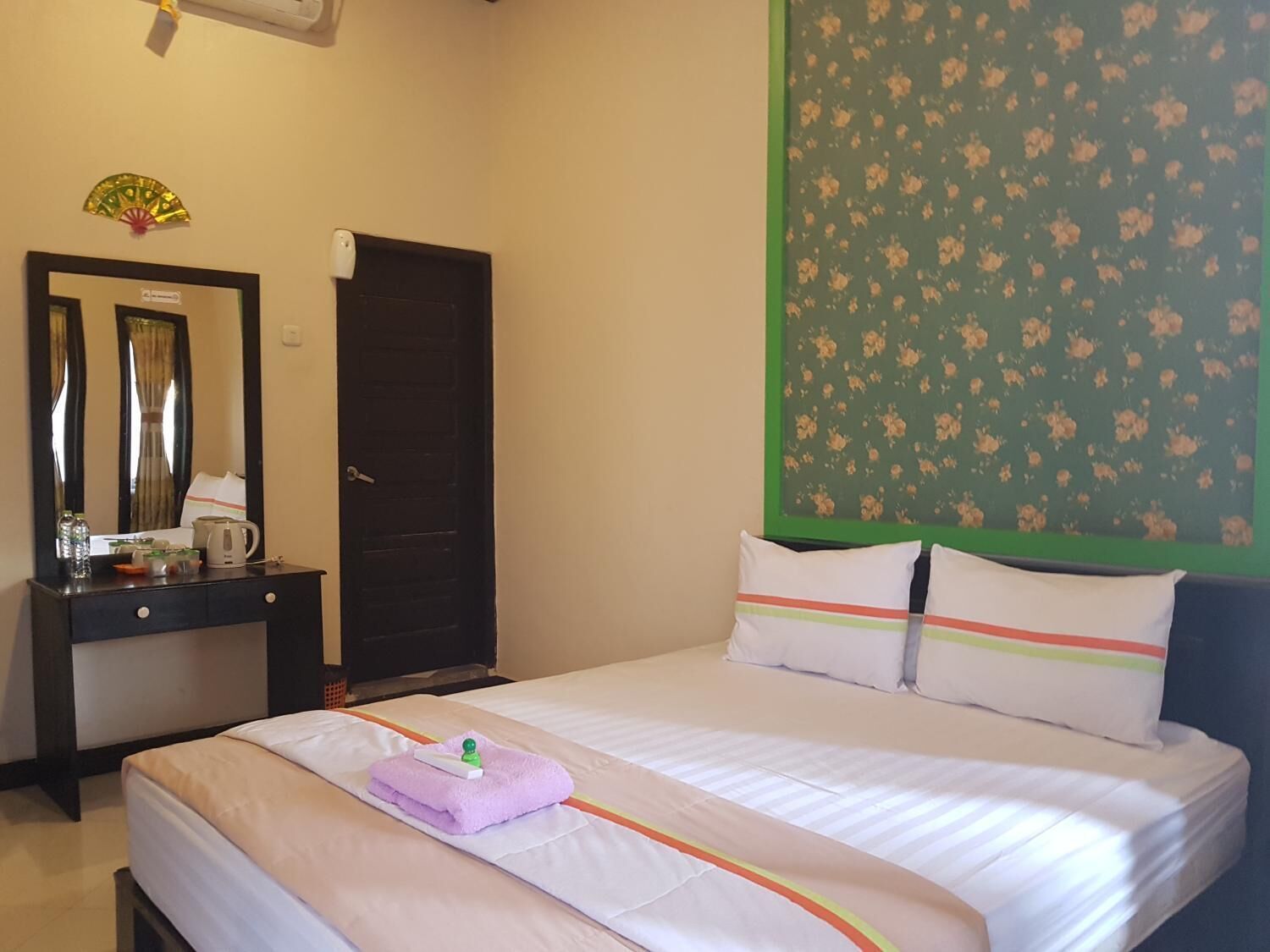 A hotel room with a bed, a dresser, a mirror, a door, and a floral wall decoration.