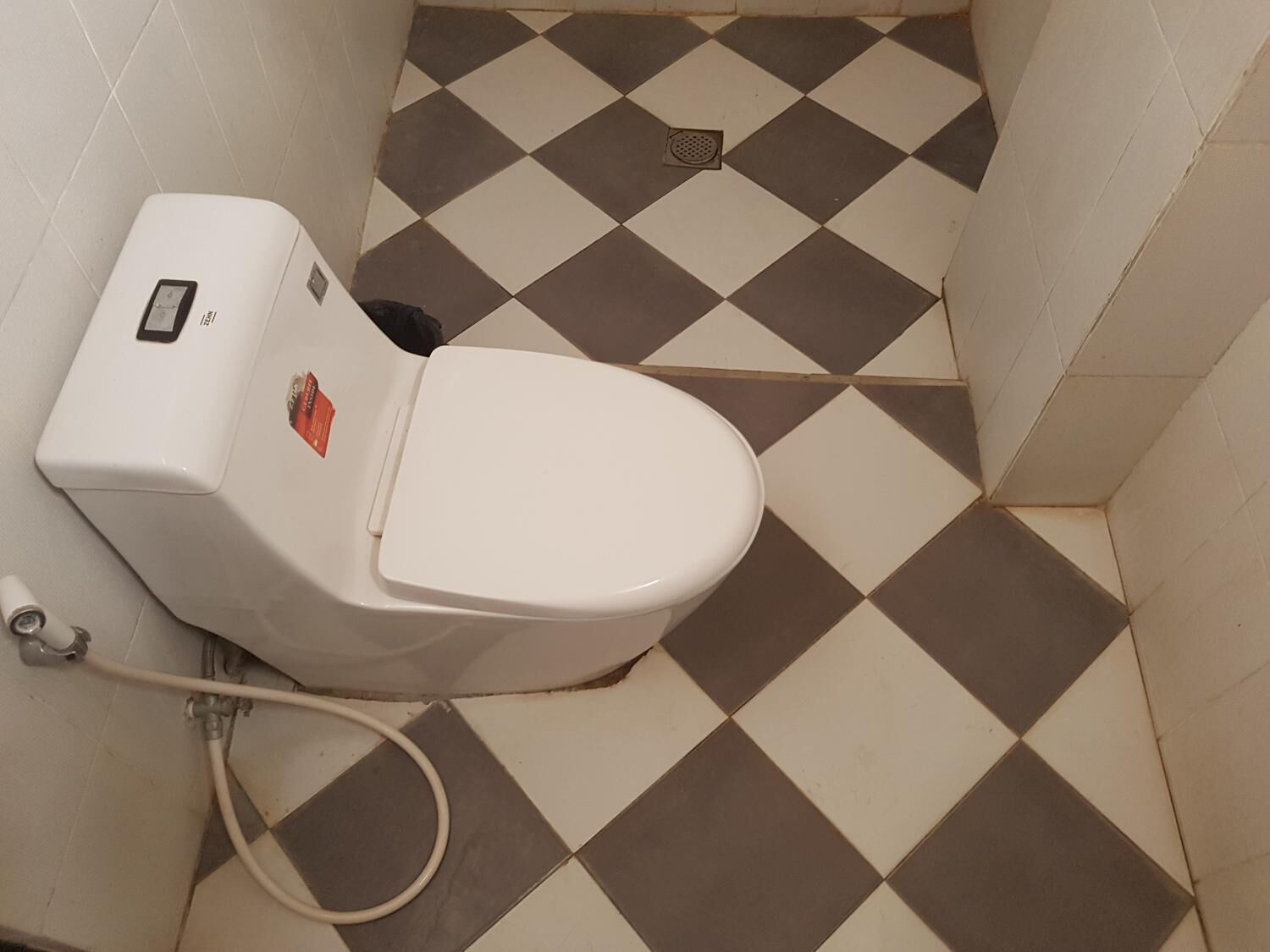 A toilet with a digital display and a bidet attachment in a bathroom with checkered tile flooring.