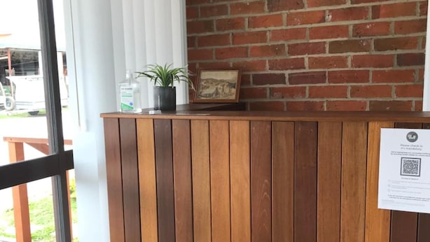A reception desk with a wooden finish, a potted plant, and a framed picture on the wall. - Royal Motel Tenterfield (Tenterfield)