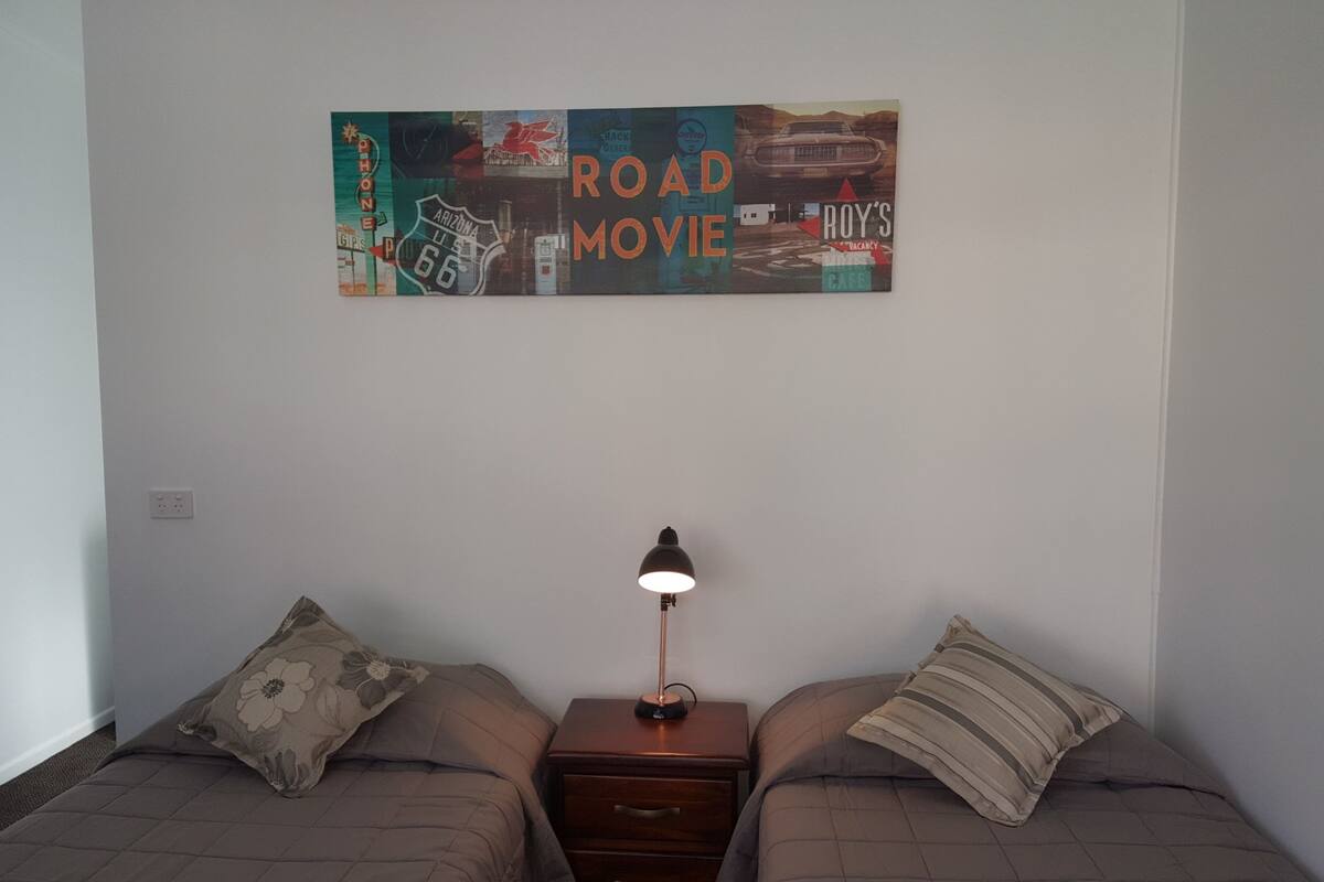 Une chambre avec deux lits, une table de chevet avec une lampe et un panneau fixé au mur.