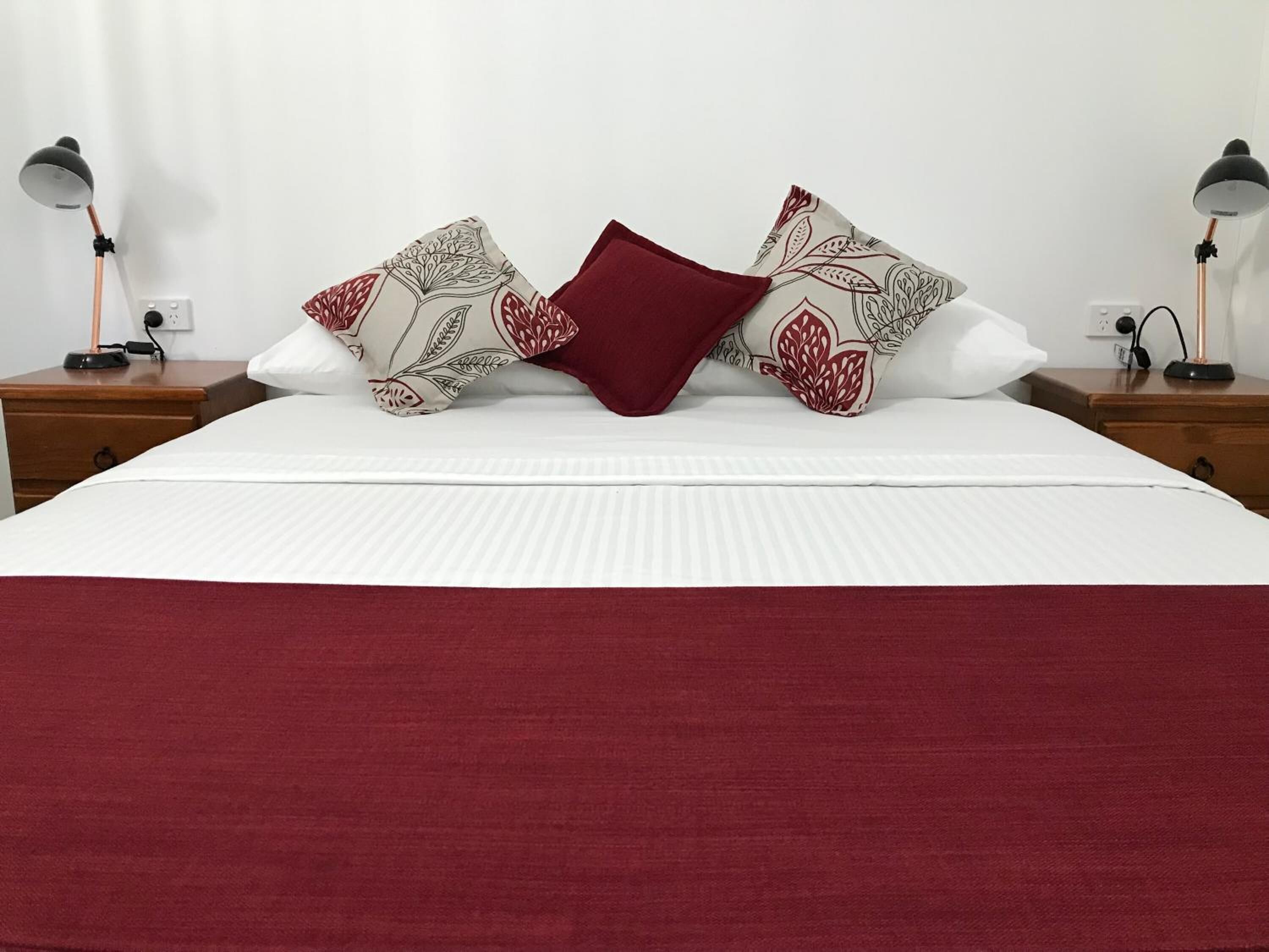 A neatly made bed with a white comforter, two patterned pillows, and a red throw blanket.