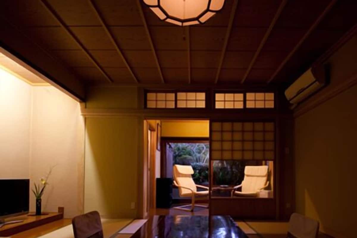 A traditional Japanese room with tatami flooring, a low table, and sliding doors leading to a garden.