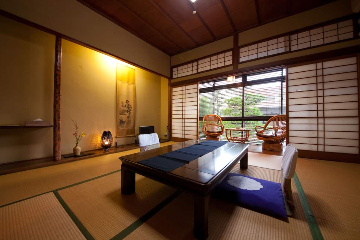 A traditional Japanese room with tatami flooring, a low table, and two wooden chairs.